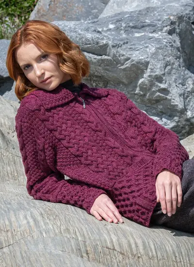 Red head model laying on rock in grace full zip aran cardigan in raspberry melange